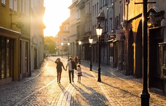 Family walking through a sunlit European cobblestone street with colorful building facades and outdoor cafés