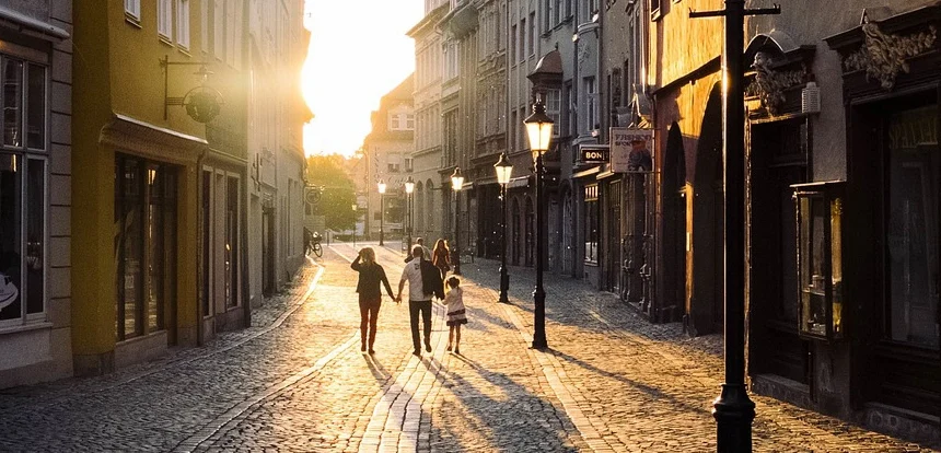 Family walking through a sunlit European cobblestone street with colorful building facades and outdoor cafés