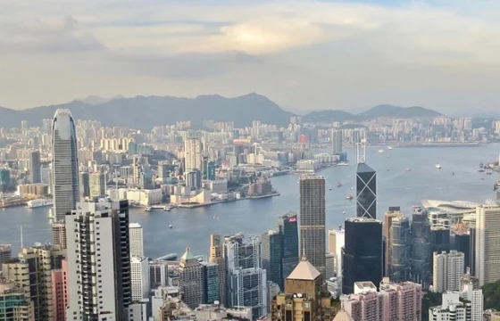 Panoramic view of Hong Kong skyline and harbor at golden hour with a traveler looking out from a high vantage point