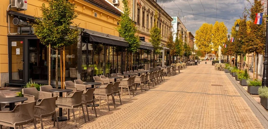 Empty European street cafe in early spring with bare budding trees and soft morning light on stone buildings