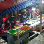 colorful dishes at a brightly lit Southeast Asian night market food stall with and other stalls in the background