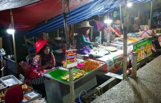 colorful dishes at a brightly lit Southeast Asian night market food stall with and other stalls in the background