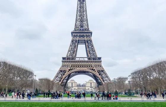 Crowds walking along a Parisian street with the Eiffel Tower rising behind them on a bright clear day
