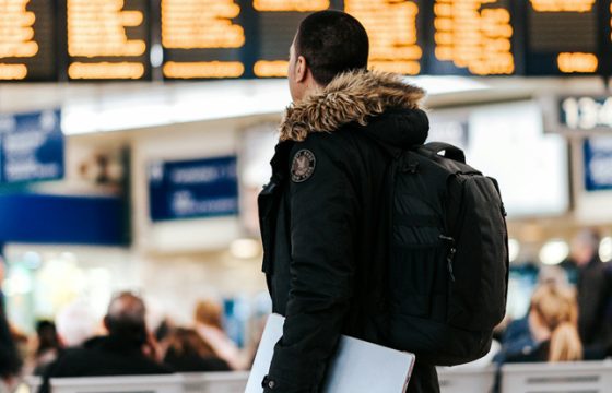 Confident traveler standing in a bright airport terminal with only a small backpack with no checked luggage