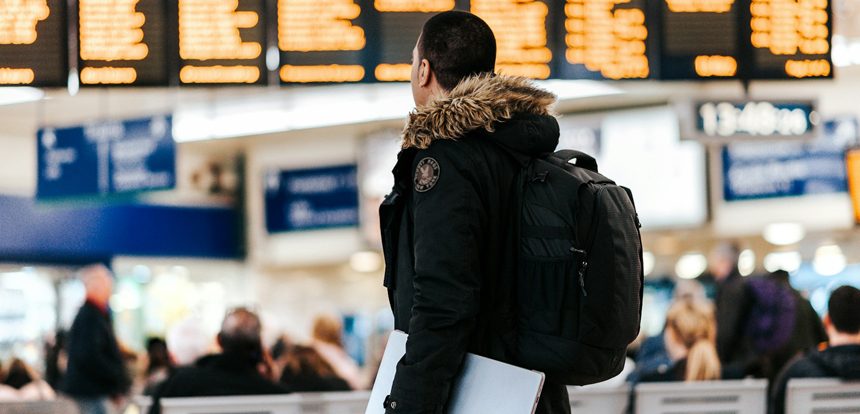 Confident traveler standing in a bright airport terminal with only a small backpack with no checked luggage