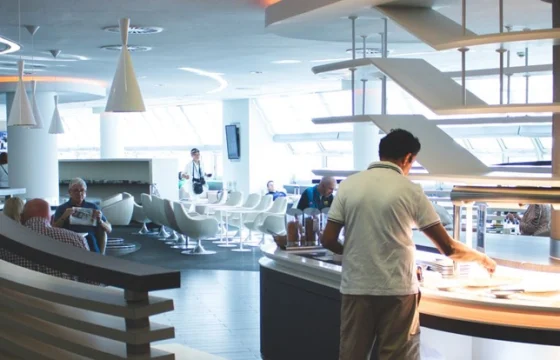 Traveler relaxing in a plush seat in a calm airport lounge with a buffet food spread and drinks bar visible