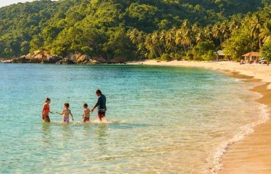 Family splashing at the shoreline of a calm turquoise tropical beach with lush green hills in the background