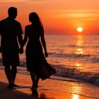 Romantic couple walking along a beach at sunset with soft warm light reflecting on calm water for their honeymoon
