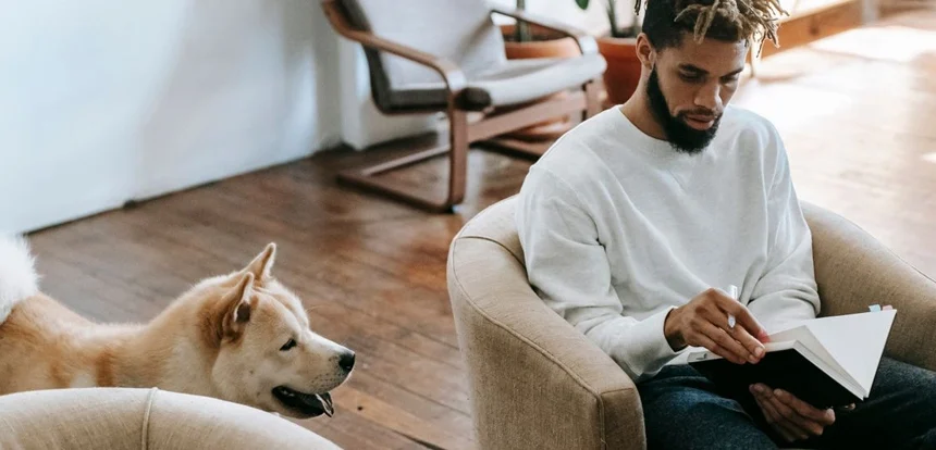 Person reading in an armchair in a comfortable living room with a dog looking